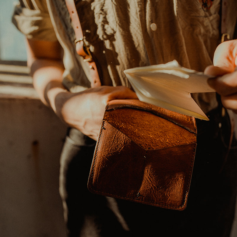 Male Model holding a Leather Wallet with folded paper inside. Leather Suspenders. Milwaukee. Directive